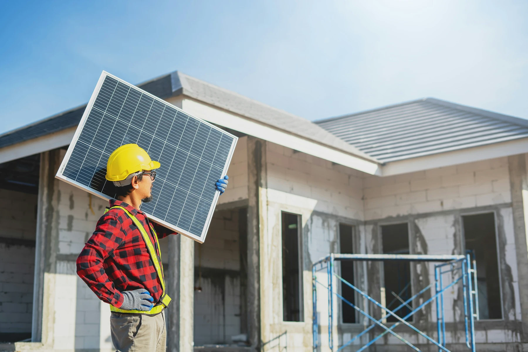 Manutention professionnelle d'un panneau solaire Installateur casqué transportant un module photovoltaïque devant une maison en chantier
