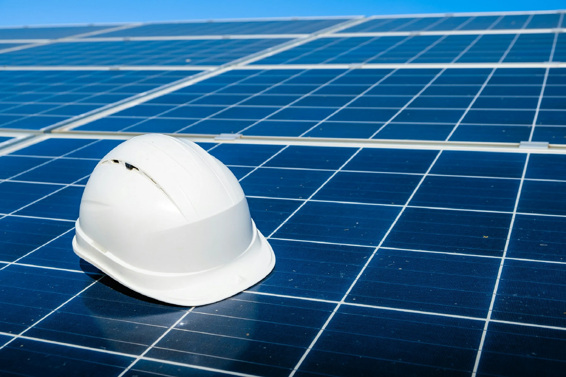 Préparer un diagnostic photovoltaïque sécurisé Casque de chantier posé sur une rangée de modules photovoltaïques